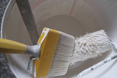Üst manzarada bir kova boya ve fırça var. Beyaz boyalı kova. Boya aletleri. Ev dekorasyonu, yeniden yapılanma.