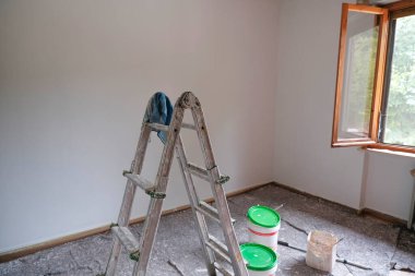 Merdiven, silindir ve boya silindiri. Boya almaya hazır boş bir odada boya kovaları. Duvarları boyamak, yeniden yapılandırma işleri.