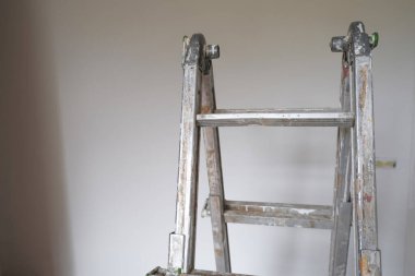 Beyaz duvarlar boyunca mavi paçavrayla boyanmış metal merdiven. Duvarları boyamak, yeniden yapılandırma işleri. Yenileme araçları