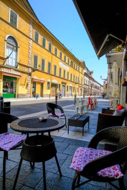 Haziran 2021 Parma, İtalya: Şehrin karşısındaki bir kafede sandalyeli masalar, sarı bina, eski kasaba, yürüyen insanlar, yol. 