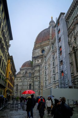December 2021 Florence, Italy: Dome of Santa Maria del Fiore, Battistero di San Giovanni, Piazza san Giovanni on a rainy day. Tourists walking with umbrellas 