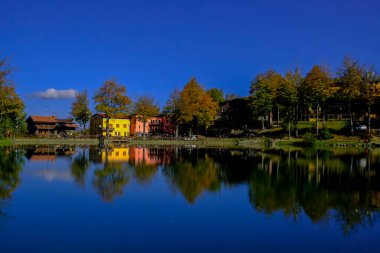Güneşli bir günde gölde renkli evler. Su yansımaları. Peyzaj arka planı. Cerreto Laghi, Reggio Emilia, İtalya. Seyahat 