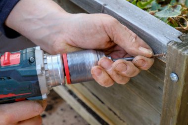 Yakın plan çekimde çalışan bir adamın elindeki delme aleti. Tahtada delik açmak. İnşaat ve inşaat ekipmanı ve çalışma