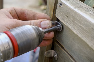 Yakın plan çekimde çalışan bir adamın elindeki delme aleti. Tahta tahtada vida vidaları. İnşaat ve inşaat ekipmanı ve çalışma