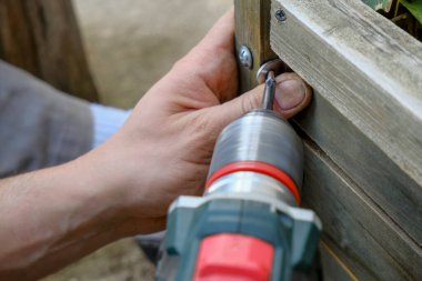 drilling tool in man's hands working close-up. Screwing bolts in wooden plank. Construction and building equipment and work