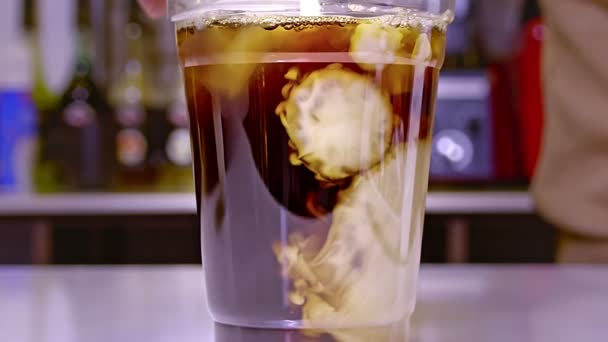 透明なプラスチックカップに牛乳とコーヒーの混合物 スローモーションショット — ストック動画