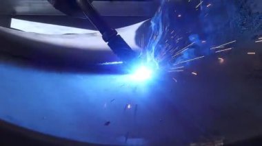Kaynak yakın çekim. Fabrika işçisinin koruyucu maskeli, metal malzemeyi meşaleyle kaynak yaparken, alevin etrafında kıvılcımlar uçuşurken yakın görüntüsü