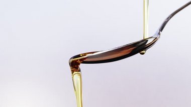 Olive oil pouring on a spoon over white background in slow motion