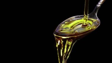 Kaşık üzerine ağır çekimde siyah arkaplan üzerine zeytinyağı dökülüyor