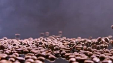 Kahve çekirdekleri siyah aynaya düşerken duman siyah arkaplanı ağır çekimde kaplıyor..