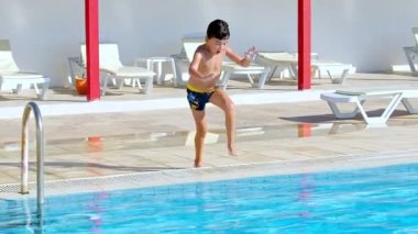 Bir çocuk havuza atladı. Çocuk suda çok eğleniyor. Yan görüş, el çekimi. Mutluluk, çocukluk, yaz, tatiller, ağır çekim.