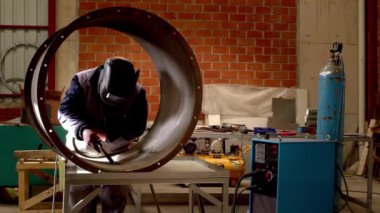 Koruyucu maske takan fabrika işçisi meşale ile metal malzemeler kaynak yapıyor; alevin etrafında uçuşan kıvılcımlar.