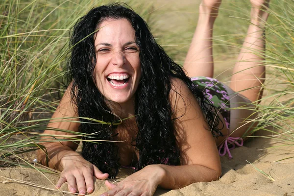 Chica en bikini riéndose en la playa en la hierba alta y arena Fotos De Stock