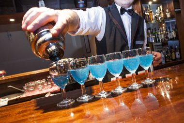 Barman pouring blue coloured drinks to the glasses on the bar co clipart
