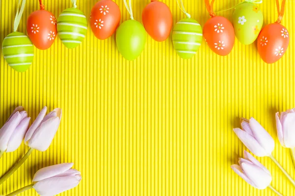 Arreglo de huevos y tulipanes de color Pascua sobre fondo amarillo — Foto de Stock