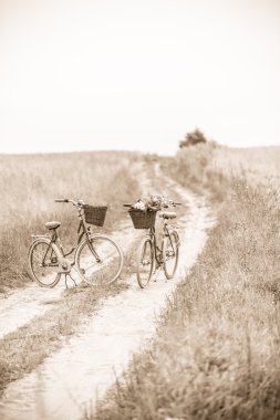 Two old style looking bikes parked on dirt road, sepia. clipart