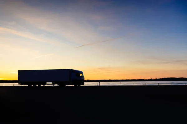 Lastbil som transporterar en behållare mot solnedgången bakgrund. Stockfoto