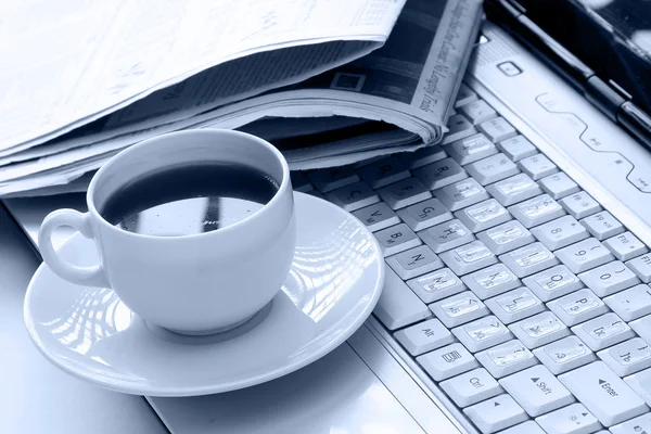 Cup of coffee and a newspaper on a laptop — Stock Photo, Image