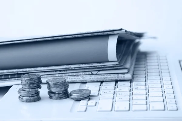 Newspapers and coins on a white laptop — Stock Photo, Image