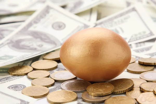 En guld ägg liggande på dollar och mynt — Stockfoto