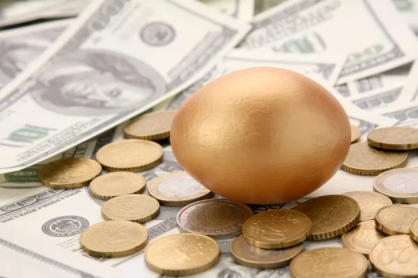 En guld ägg liggande på dollar och mynt — Stockfoto