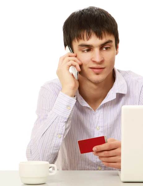 Hombre con tarjeta de crédito y teléfono delante de un portátil — Foto de Stock