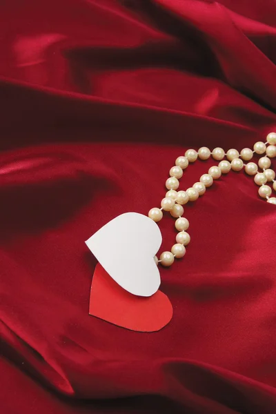 Hearts with pearls on red silk — Stock Photo, Image