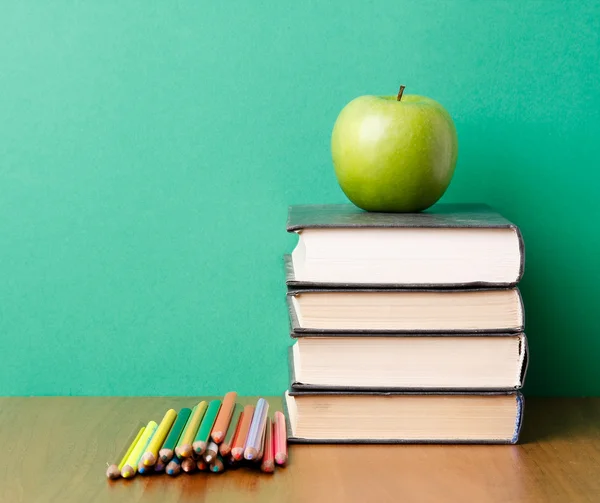 Green apple on a pile of books and pencils — Stock Photo, Image