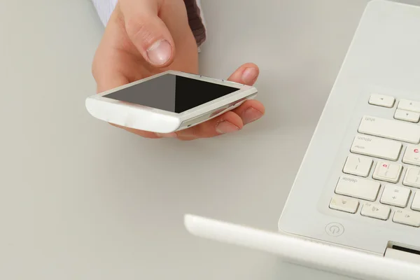 Touchphone dans une main masculine, près d'un ordinateur portable — Photo