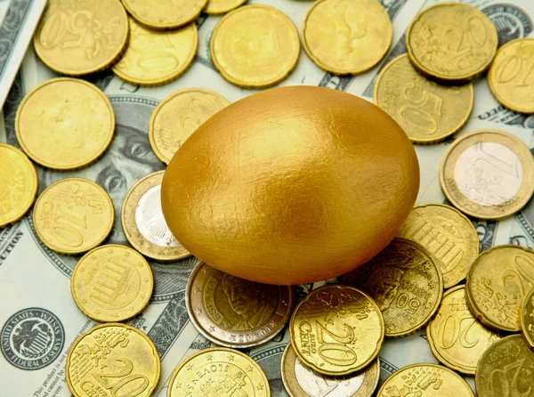 Złote jajko leżące na dolary i monety — Zdjęcie stockowe