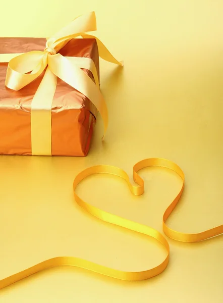 A gift and a yellow ribbon shaping heart. — Stock Photo, Image