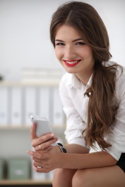 İş kadını ofiste oturan akıllı telefonuyla mesaj gönderiyor.