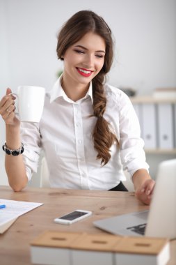 Genç bir iş kadını ofisinde fincanla masada oturuyor.