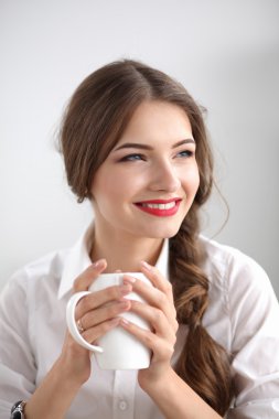 Genç bir iş kadını ofisinde fincanla masada oturuyor.