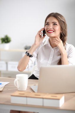 Genç iş kadını masada oturuyor ve telefonla konuşuyor.