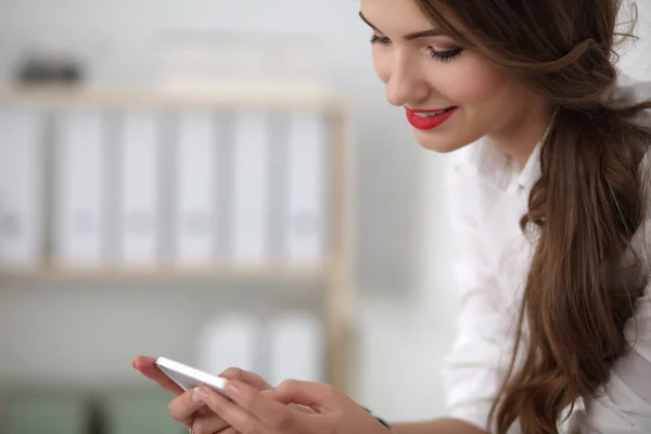Businesswoman sending message with smartphone sitting in the office — Stock Photo, Image