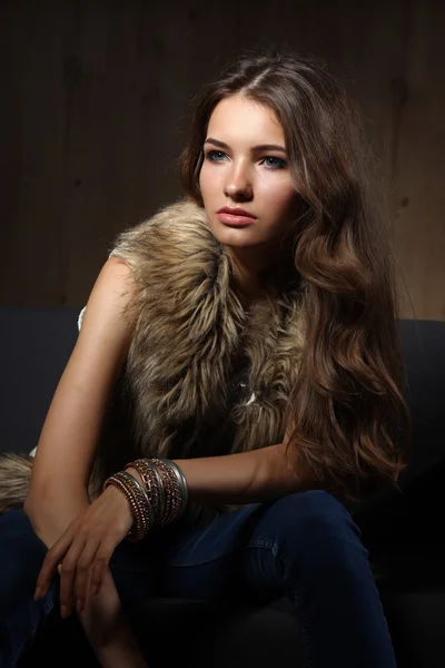 Retrato de mulher elegante sentado no sofá preto vestindo uma calça azul e colete de pele — Fotografia de Stock