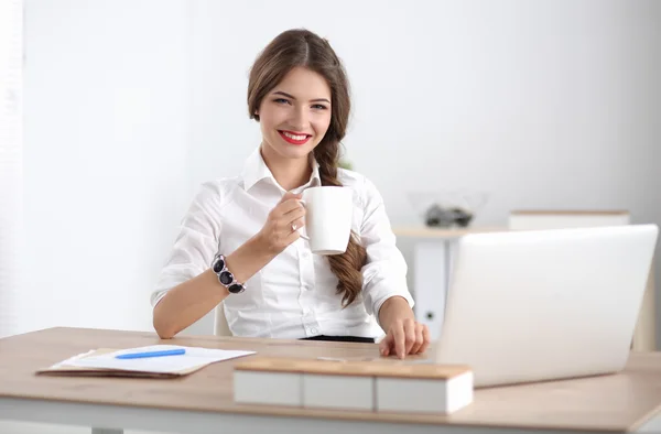Jovem empresária sentada na mesa com xícara no escritório — Fotografia de Stock