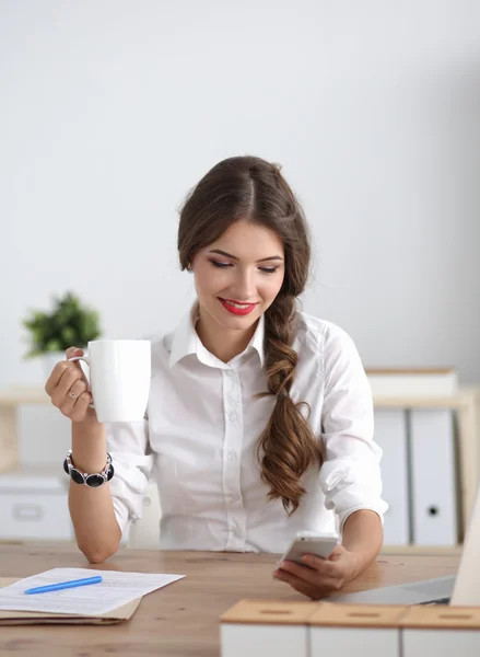 Junge Geschäftsfrau sitzt mit Tasse im Büro auf dem Schreibtisch — Stockfoto