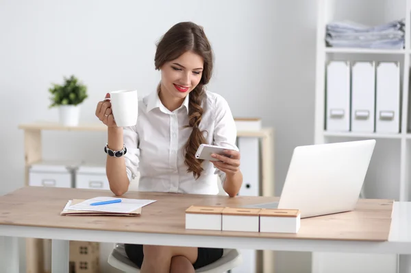 Młoda bizneswoman siedzi na biurku z filiżanką w biurze — Zdjęcie stockowe
