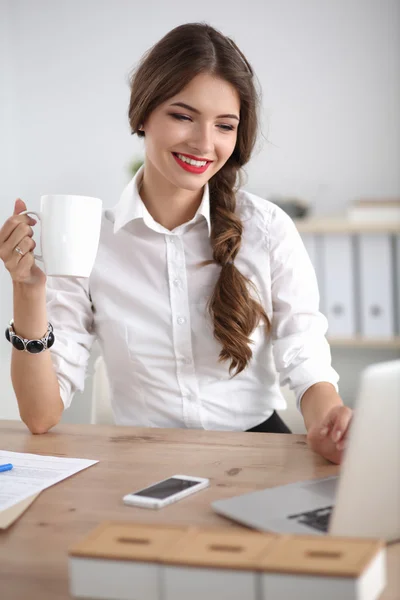 Jovem empresária sentada na mesa com xícara no escritório — Fotografia de Stock