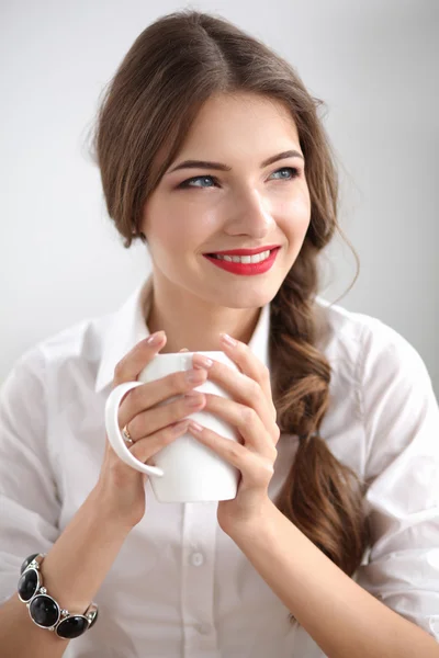 Young businesswoman sitting on the desk with cup in office — Stock Photo, Image