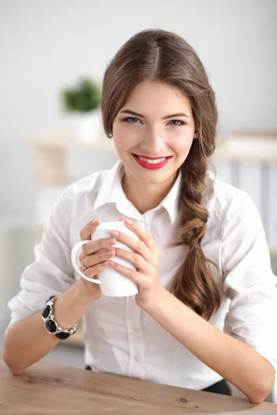 Junge Geschäftsfrau sitzt mit Tasse im Büro auf dem Schreibtisch — Stockfoto