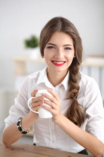 Молодая деловая женщина сидит на столе с чашкой в офисе — стоковое фото
