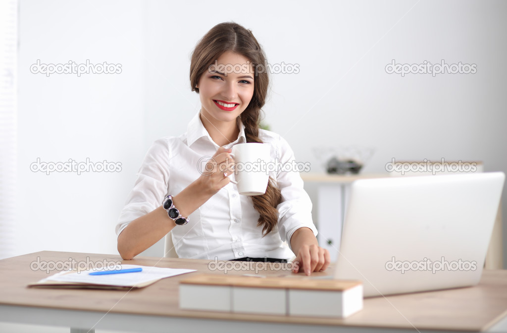 Young businesswoman sitting on the desk with cup in office