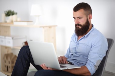 Yakışıklı genç adam dizüstü bilgisayarda oturuyor ve çalışıyor..