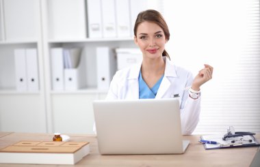 Kadın doktor masada oturuyor ve hastanede dizüstü bilgisayarla çalışıyor.