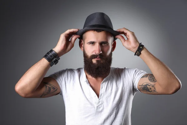 Retrato de hombre barbudo guapo con sombrero de pie, aislado sobre fondo gris — Foto de Stock