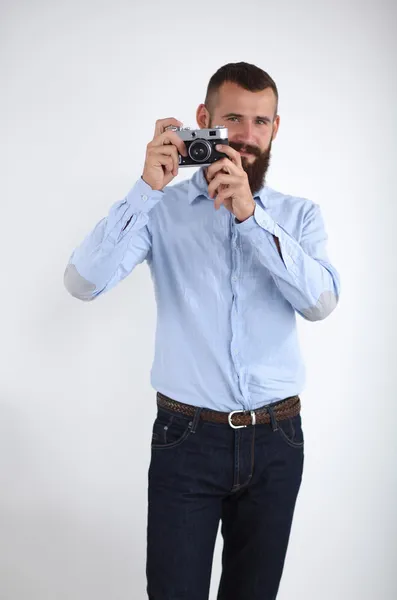 Junger Mann mit Bart fokussiert dich mit seiner Kamera, während du vor weißem Hintergrund stehst — Stockfoto