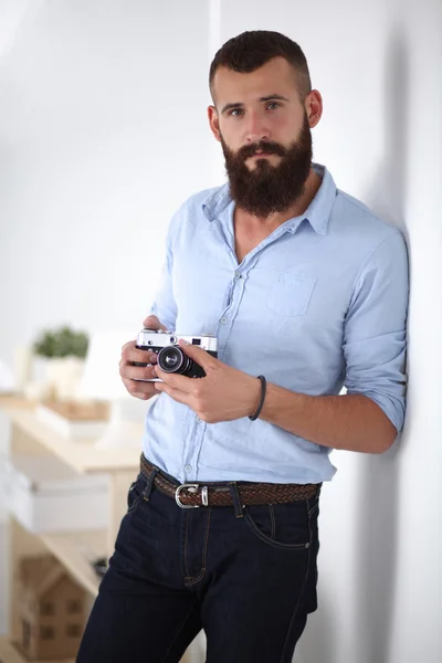 Joven barba hombre sosteniendo una cámara mientras está de pie sobre fondo blanco — Foto de Stock